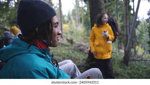 Group of travelers resting in camp after long walking trek in the mountains. Multiethnic young hikers talking, having snack in the forest during tourist trip or hike in autumn. Active leisure concept.