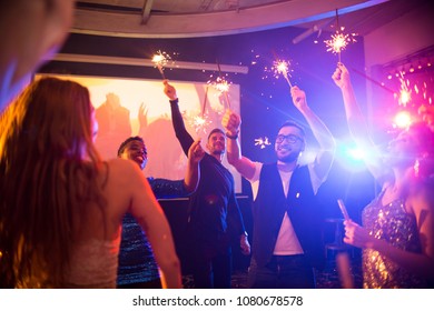 Group of trendy young people celebrating holiday in nightclub burning flaming sparklers on dance floor, copy space - Shutterstock ID 1080678578