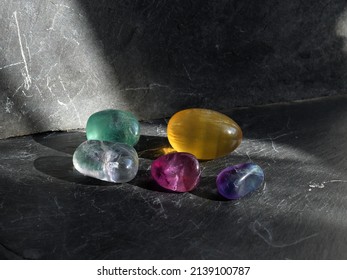 Group of tumbled fluorite  pebbles in different colors , on gray slate background, lit by the sun