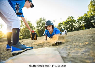 Group Of Two Baseball Players Play Together On The Playground. On Of Them Slide On The Goal