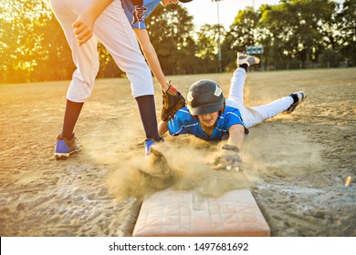 Group Of Two Baseball Players Play Together On The Playground. On Of Them Slide On The Goal