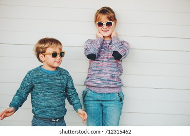 Group Of Two Funny Kids Playing Together Outside, Little Boy And Girl Posing Against White Wooden Background, Brother And Sister Wearing Matching Pullovers, Fashion For Children, Knitwear.