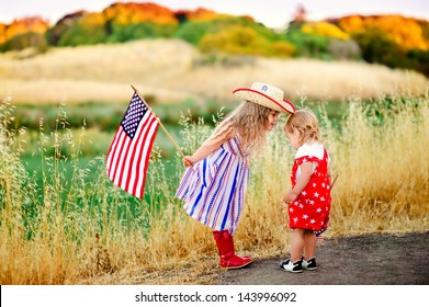 group of two happy adorable little kid girls smiling and waving American flag outside, his dress with strip and stars, cowboy hat. Smiling child celebrating 4th july - Independence Day - Powered by Shutterstock