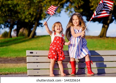 group of two happy adorable little kid girls smiling and waving American flag outside, his dress with strip and stars, cowboy hat. Smiling child celebrating 4th july - Independence Day - Powered by Shutterstock