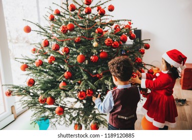 Group Of Two Little Children Playing With Christmas Tree At Home