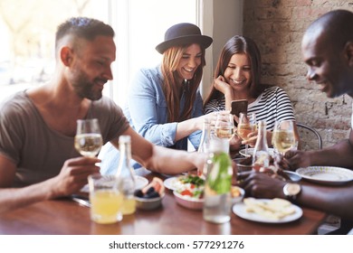 Group Of Two Male And Two Female Having Delicious Dinner While Girls Sharing Something On Phone. 