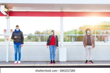 Group Of Two Men And A Woman Wearing Protective Face Mask In A Train Station Waiting For The Bus Keeping Social Distances. People Standing On A Metro Stop After Reopening Post Lockdown. New Normal 