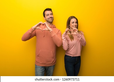 Group Of Two People On Yellow Background Making Heart Symbol By Hands