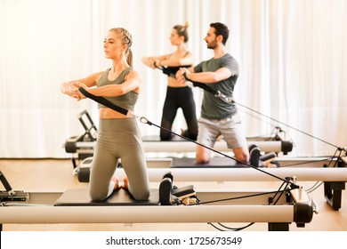 Group Of Two Women And A Man Doing Torsion Rotation Exercises During A Class Using Pilates Reformer Beds In A High Key Gym With Copy Space In An Active Lifestyle And Fitness Concept