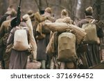 Group of unidentified re-enactors dressed as World War II Russian Soviet soldiers in camouflage walks through forest.