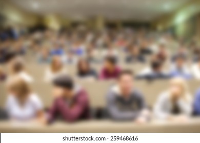 Group of university students attentively listening to the teacher during lectures in the hall. Blurred in post processing; abstract background.
