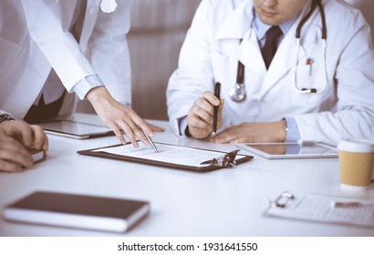 Eine Gruppe unbekannter Ärzte sitzt am Schreibtisch und diskutiert die medizinische Behandlung mit einem Zwischenablage, Nahaufnahme. Team von Ärzten am Arbeitsplatz in einer Klinik. Konzept der Medizin und des Gesundheitswesens