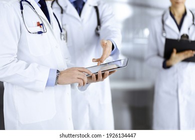 Eine Gruppe unbekannter Ärzte benutzt eine Computertablette, um einige Patientenakten zu überprüfen, während sie im Krankenhausbüro stehen. Ärzte, die bereit sind, Patienten zu untersuchen und zu helfen. Medizinische Hilfe, Versicherung in
