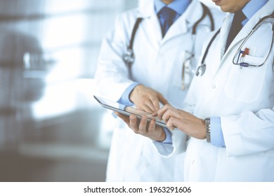 Group of unknown doctors use a computer tablet to check up some medical names records, while standing in a hospital office. Physicians ready to examine and help patients. Medical help, insurance in - Shutterstock ID 1963291606