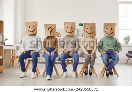 Group of unknown people put paper shopping package bags with emoticons on their heads. People sit in row and wear positive emoticons, one of them sits with unknown emotion and wears question mark.