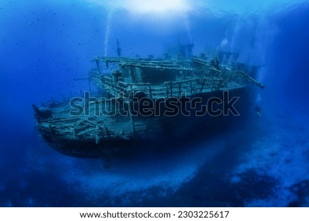 A group of unrecognizable divers explore a big, sunken shipwreck in the blue, mediterranean sea at Naxos island, Greece