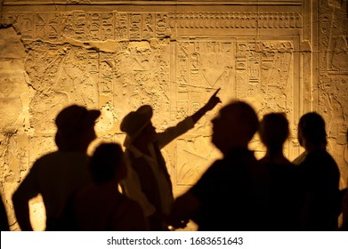 Group of unrecognizable tourist archeologists standing in silhouette in front of ancient Egyptian hieroglyphs