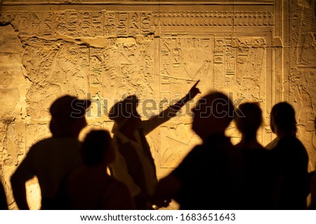 Group of unrecognizable tourist archeologists standing in silhouette in front of ancient Egyptian hieroglyphs