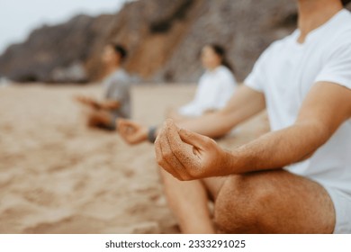 Group of unrecognizable young people meditating together, sitting in lotus position and hands in mudra gestures, practising yoga on beach, closeup - Powered by Shutterstock