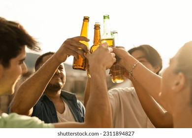 A group of unrecognizable young people toast downtown with glass bottles on the roof of an open-air apartment. A close-up of a multiracial group toasting with beers. Concept of multiracial youth.