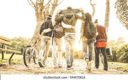 Group of urban friends walking in city skate park with backlighting at sunset - Youth and friendship concept with multiracial young people having fun together - Warm retro filter with soft focus