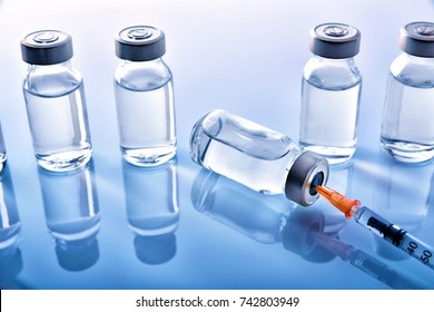 Group of vials with medication and punctured syringe on blue methacrylate table. Horizontal composition. Elevated view.