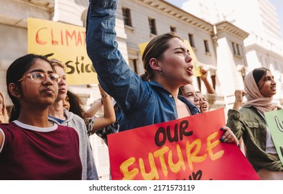 Group of vibrant youth activists raising banners and shouting slogans during a climate change protest. Multicultural young people marching for climate justice and environmental sustainability. - Shutterstock ID 2171573119