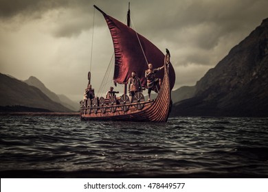 Group Of Vikings Are Floating On The Sea On Drakkar With Mountains On The Background.