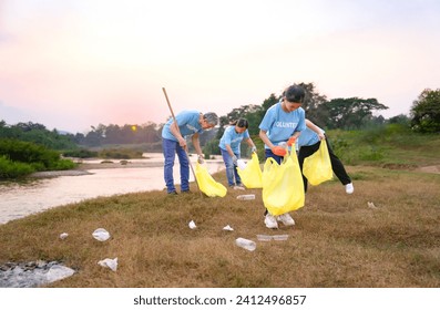 group of volunteers in blue t-shirt collecting garbage and sorting plastic waste, voluntary family team cleanup dirty public area full of garbang by the river in the evening sun - Powered by Shutterstock