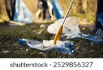 Group of volunteers cleaning the forest from litter and plastic waste, grabbing trash and junk with a long claw tool. Environmental activists picking up rubbish. Close up. Camera B.