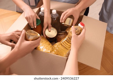 Group of volunteers packing food products at wooden table, closeup