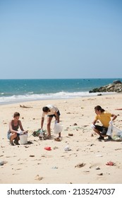 Group of volunteers picking up plastic trash in bags when cleaning sandy beach on Earth day