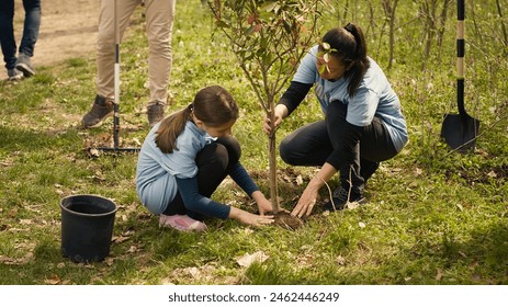 Group of volunteers planting new seedlings around the forest area, digging up holes and installing trees seeds for nature conservation and protection. Mother and little girl take action. Camera A. - Powered by Shutterstock