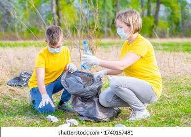 Group Of A Volunteers  Wearing Medical Protective Masks Pick Up Plastic Bottle In Summer Park. Volunteer And Ecology Concept