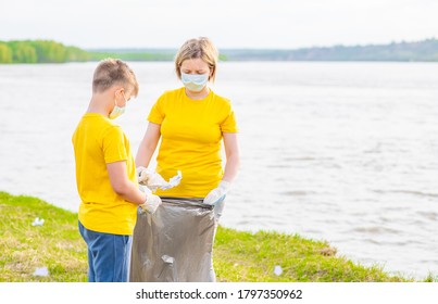 Group Of A Volunteers  Wearing Medical Protective Masks Pick Up Plastic Bottle On River Side. Volunteer And Ecology Concept. Empty Space For Text