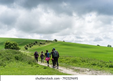 Group Walking The South Downs Way, Sussex. A Winding Path Passes Fresh Green Fields On A Stormy, Overcast, Spring Day.