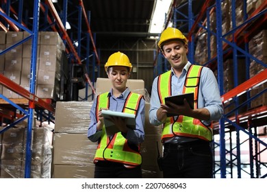 Group Of Warehouse Workers With Hardhats And Reflective Jackets Using Tablet, Walkie Talkie Radio And Cardboard While Controlling Stock And Inventory In Retail Warehouse Logistics, Distribution Center