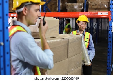 Group Of Warehouse Workers With Hardhats And Reflective Jackets Wrapping Boxes In Stretch Film Parcel On Pallet While Control Stock And Inventory In Retail Warehouse Logistics Distribution Center