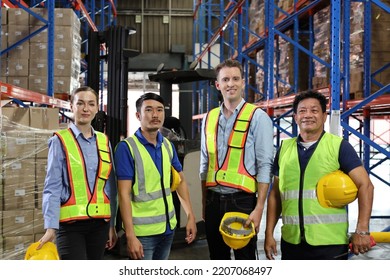 Group Of Warehouse Workers With Hardhats And Reflective Jackets Standing And Looking Camera With Confident Celebrate Successful Together Or Completed Deal At Retail Warehouse Logistics Center