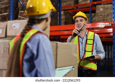 Group Of Warehouse Workers With Hardhats And Reflective Jackets Using Tablet, Walkie Talkie Radio And Cardboard While Controlling Stock And Inventory In Retail Warehouse Logistics, Distribution Center