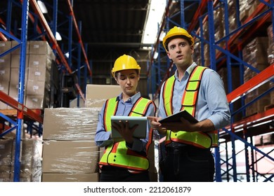 Group Of Warehouse Workers With Hardhats And Reflective Jackets Using Tablet, Walkie Talkie Radio And Cardboard While Controlling Stock And Inventory In Retail Warehouse Logistics, Distribution Center