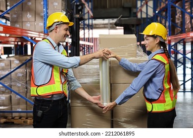 Group Of Warehouse Workers With Hardhats And Reflective Jackets Wrapping Boxes In Stretch Film Parcel On Pallet While Control Stock And Inventory In Retail Warehouse Logistics Distribution Center