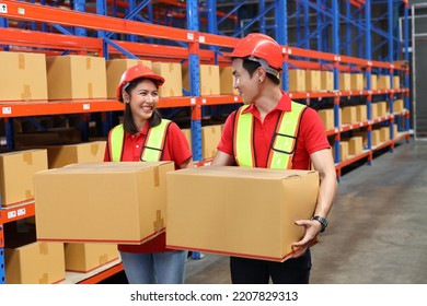 Group Of Warehouse Workers Man And Woman With Hardhats And Reflective Jackets Carrying A Large Box For Delivery To Production Stock And Inventory In Retail Warehouse Logistics, Distribution Center