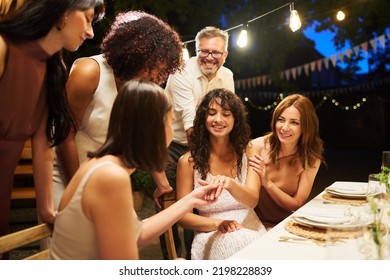 Group Of Wedding Guests Bending Over One Of Lesbian Brides Boasting With Ring On Her Finger During Feast In Luxurious Restaurant