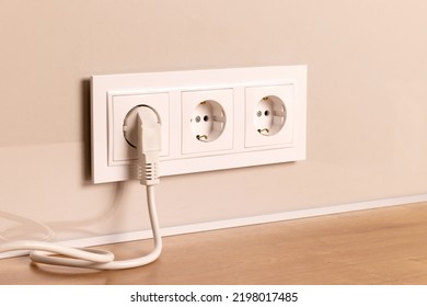 Group of white european electrical outlets with plug inserted into it on modern beige wall. Selective focus