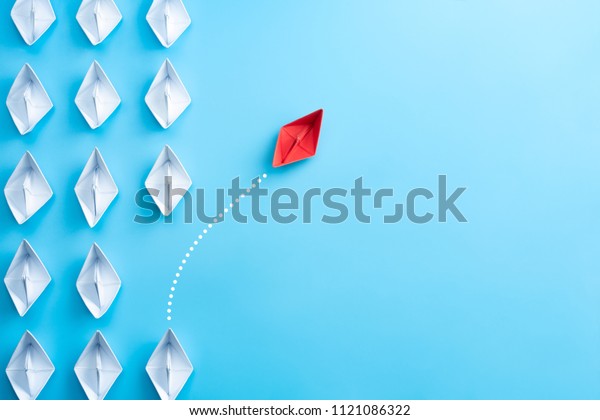 Group of white paper ship in\
one direction and one red paper ship pointing in different way on\
blue background. Business for innovative solution\
concept.