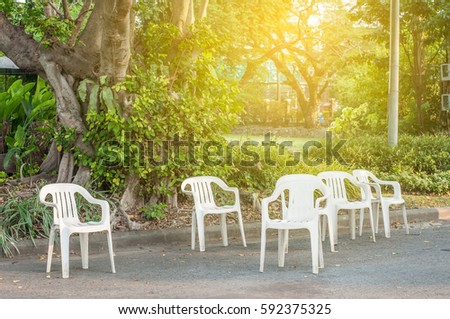 Group of white plastic chairs in green park with light flare.