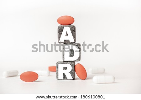a group of white and red pills and cubes with the word ADR Adverse drug reaction on them, white background. Concept carehealth, treatment, therapy.