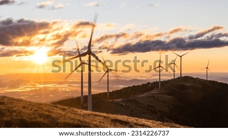 A group of wind mills on a mountain ridge in front of a morning sky during sunrise in Austria