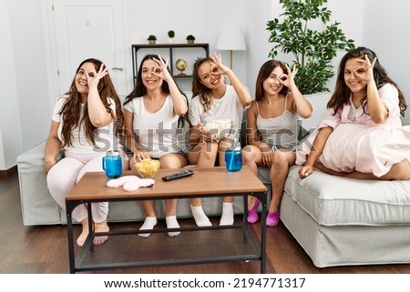 Group of women celebrating pajamas party at home smiling happy doing ok sign with hand on eye looking through fingers 